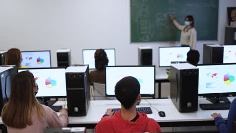 multiracial young students and teacher wearing safety face masks during coronavirus outbreak inside computer class room at university