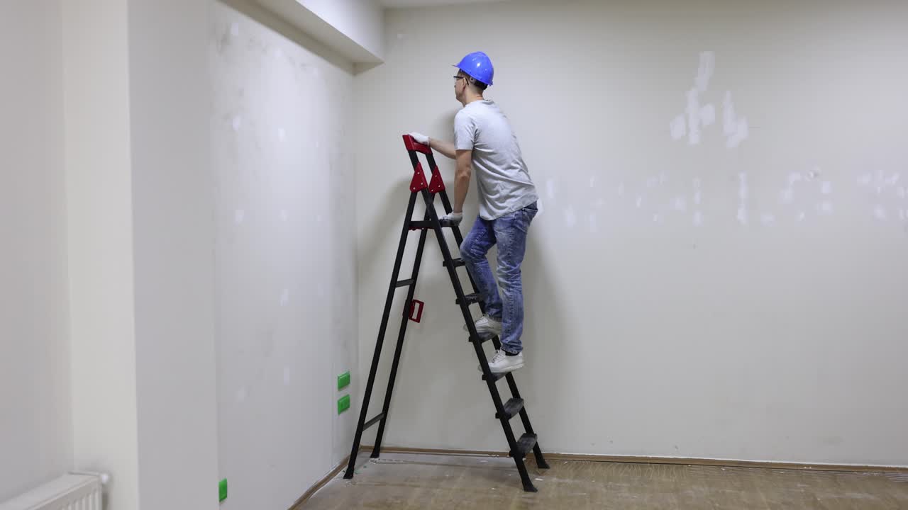 Male builder climbs to top of construction ladder in premise