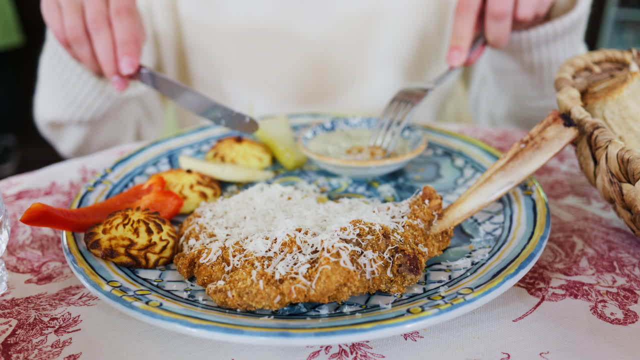 Close up of a woman cutting a piece of paneed meat and dipping it in sauce at a restaurant