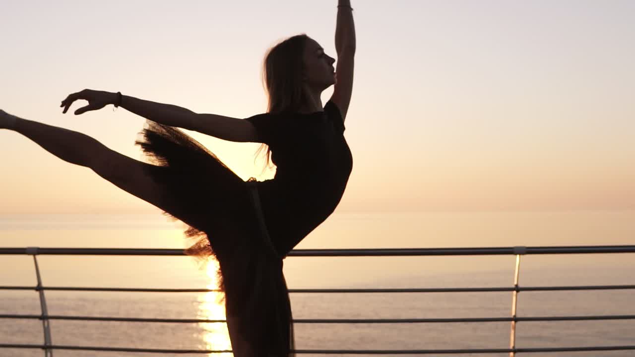Beautiful scene of a dancing ballerina in tutu and pointe near ocean or sea at sunrise or sunset. Young sensual woman with long hair practicing classic exercises.Slow motion