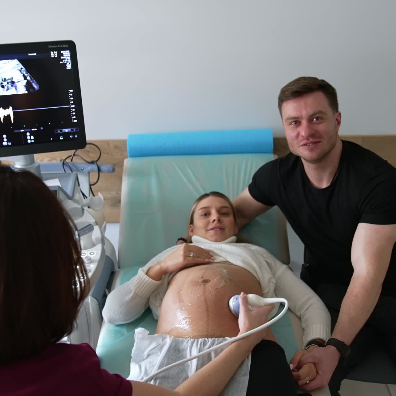 Husband supporting his pregnant child at doctor's examination. Doctor performs the ultrasound check for expecting mom