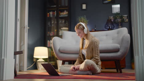 happy young woman with wireless headphones watching a funny movie on laptop computer while sitting on floor at home