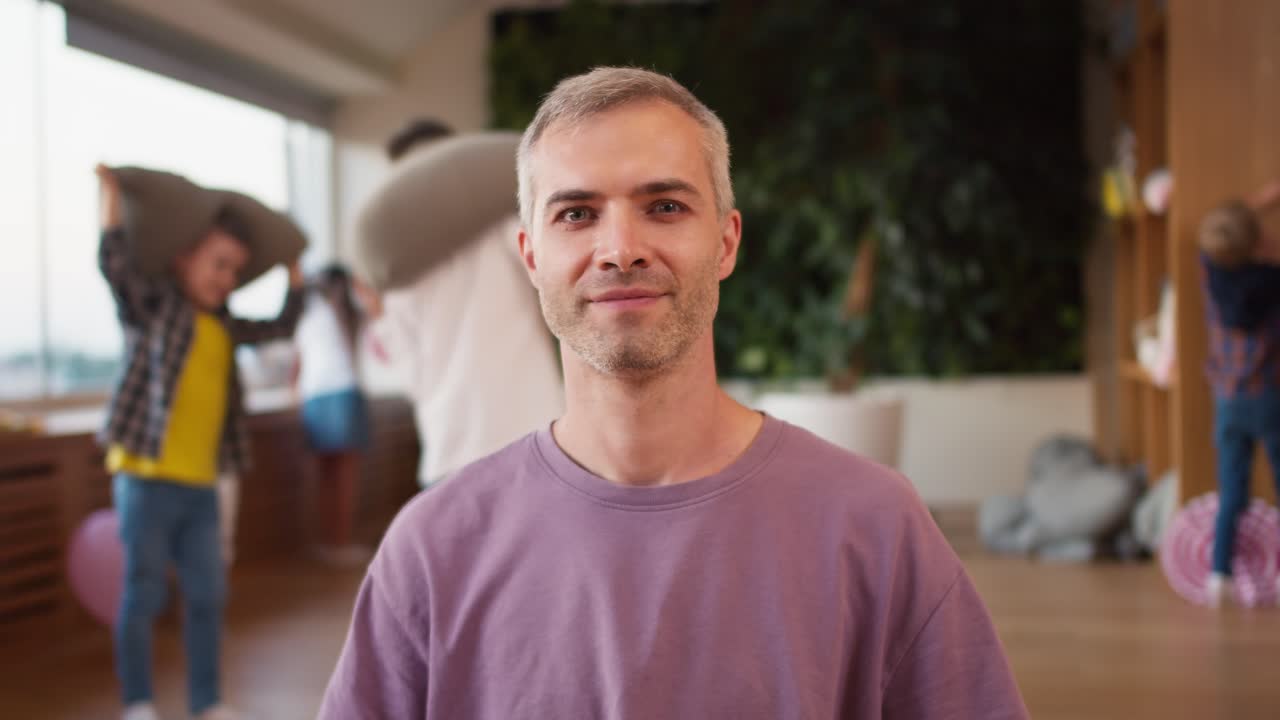 Portrait of a happy man with gray hair teacher in a purple T-shirt who poses and looks at the camera during a break in a children's school preparation club