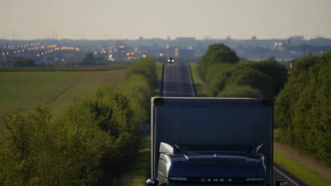 truck on a long road towards distant city lights at dusk