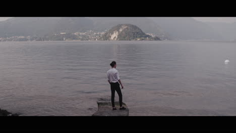 man standing on a pier overlooking a lake with mountains