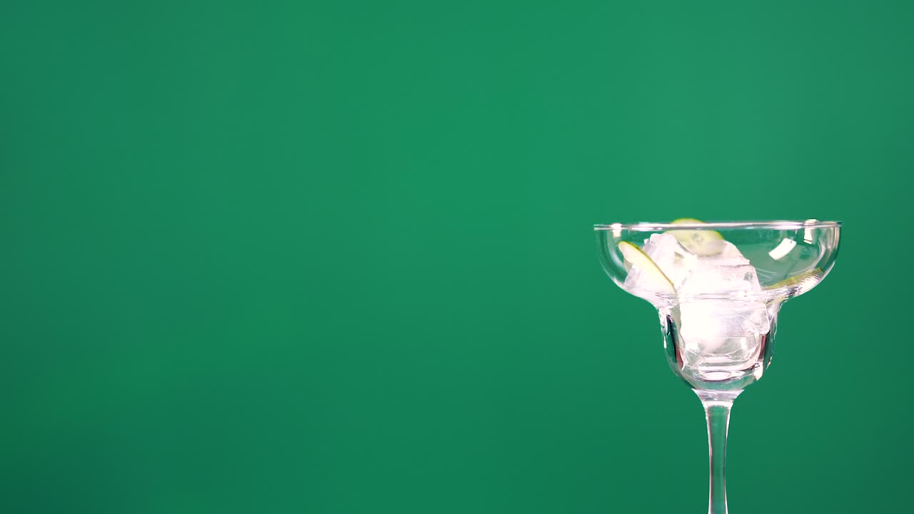 A cocktail glass with ice and lime rotates against a green screen backdrop, showcasing dynamic motion and vibrant colors