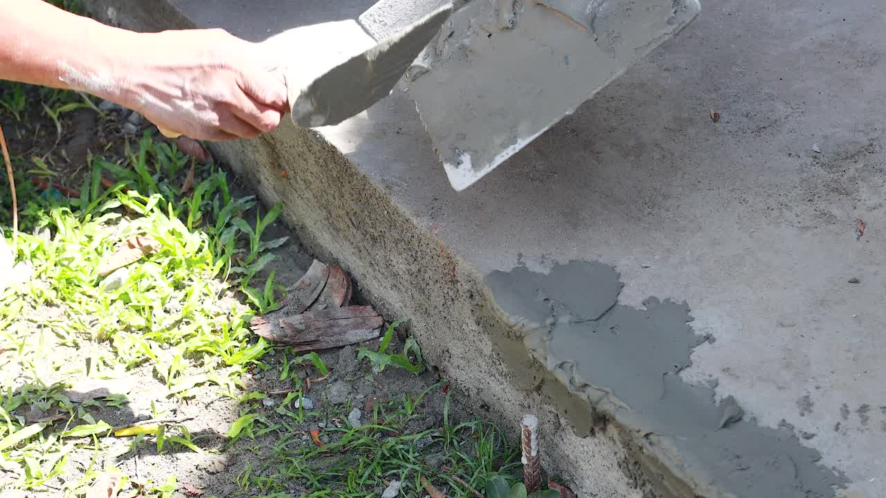 A worker smooths wet concrete on a curb in daylight, showcasing precise craftsmanship and attention to detail