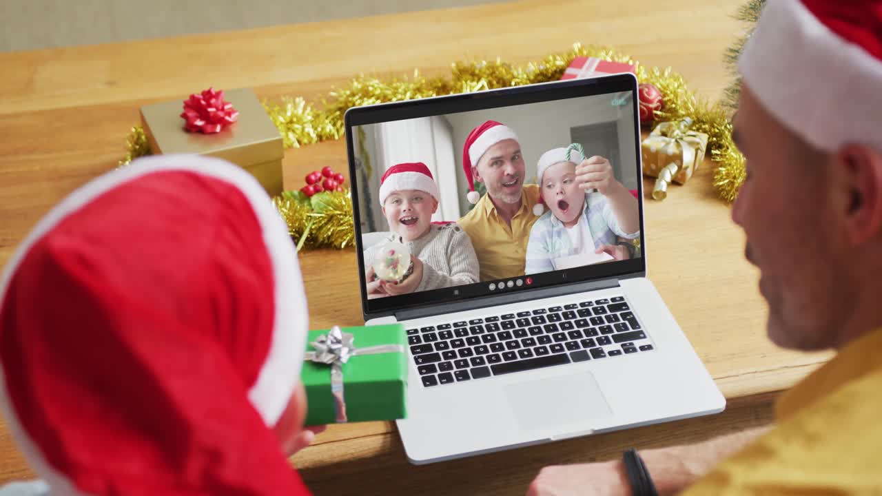 padre y hijo caucásicos con sombreros de santa usando una computadora portátil para una videollamada de navidad con la familia en la pantalla