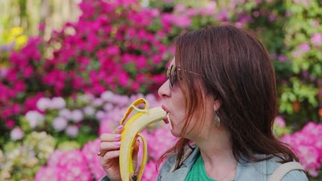 close up slow motion of mature woman enjoying banana in colorful rhododendrons