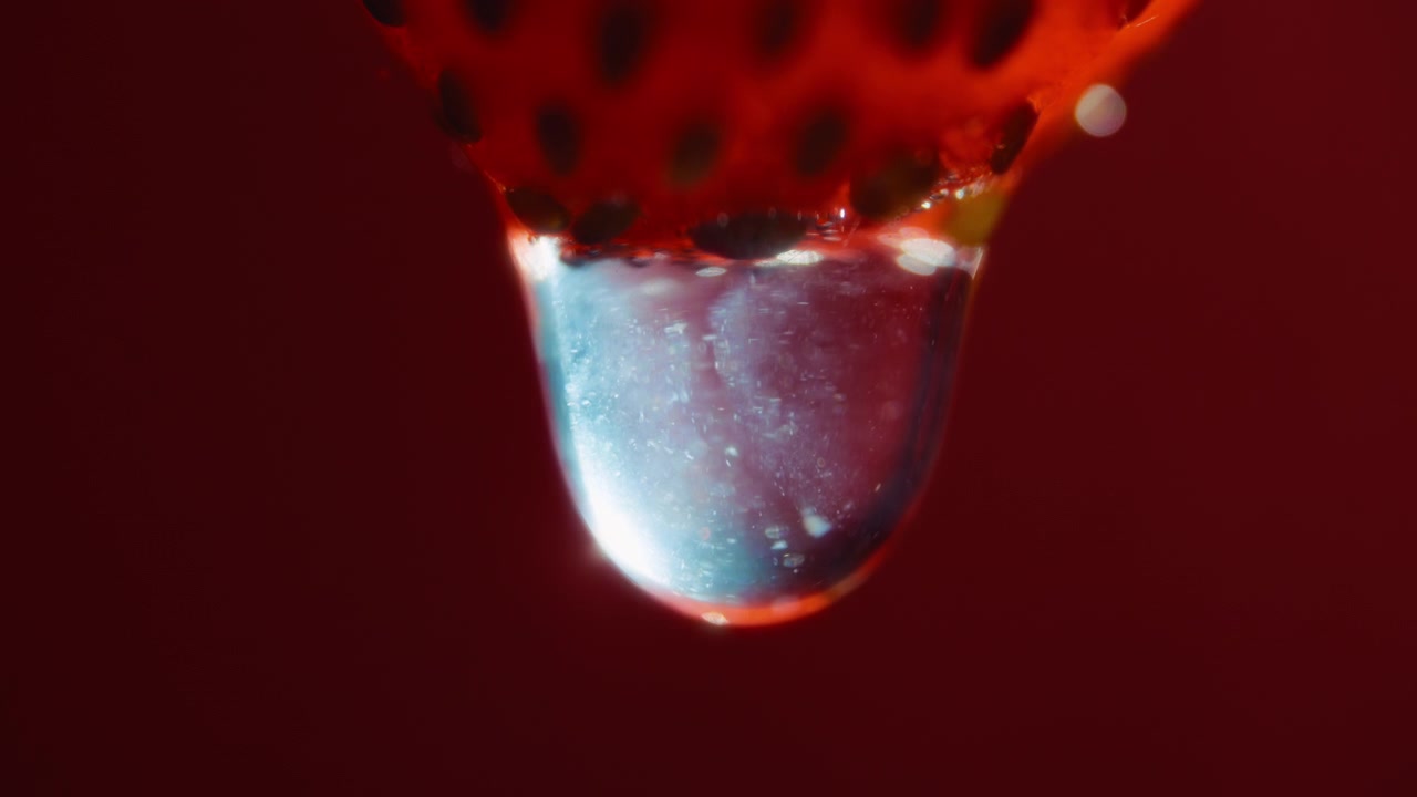 Primo piano macro di una goccia d'acqua che cade da una fragola. Movimento rallentato
