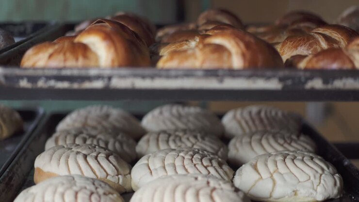 Close-up of multiple trays filled with assorted baked pastries cooling on racks inside a bakery