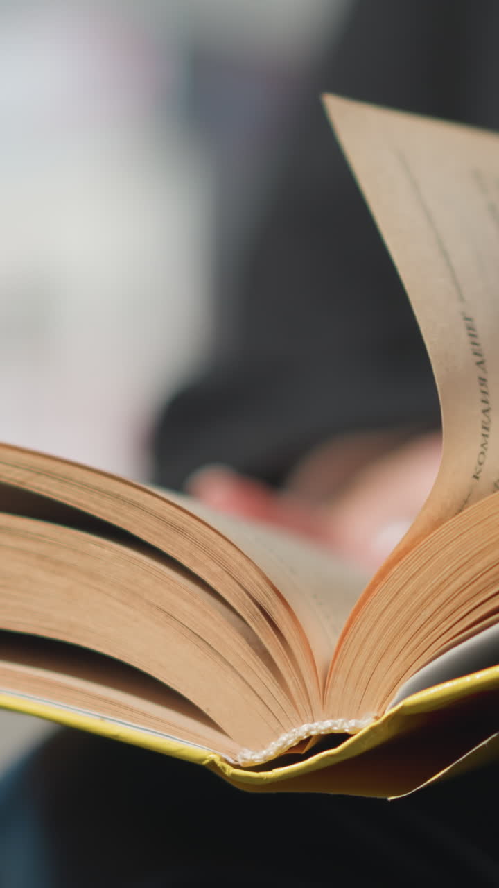 primer plano de una página de un libro siendo volteada por una mano con uñas pulidas borrosas y un anillo, vestido de negro, contra un fondo borroso
