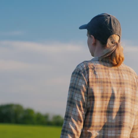 Back-View-:-Female-Farmer-Walks-Among-Wheat-Fields-On-A-Clear-Summer-Day