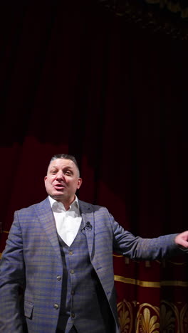 senior male entertainer dances on stage in front of theater hall. speaker akes audience laugh. entertainment concept. vertical video