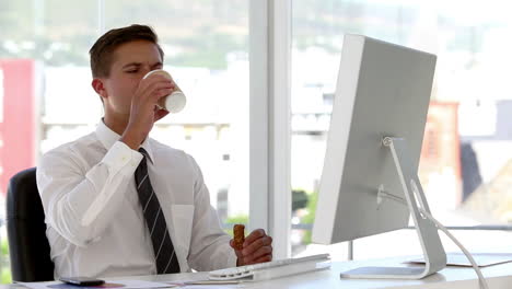 joven empresario comiendo y bebiendo mientras trabaja en su computadora