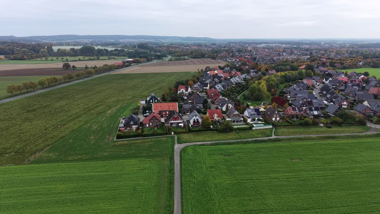 European rural suburb neighborhood with green farmland fields and single family houses. Aerial lateral wide shot. Cloudy fall day in October. Germany, Europe. Panorama view. Quiet scene