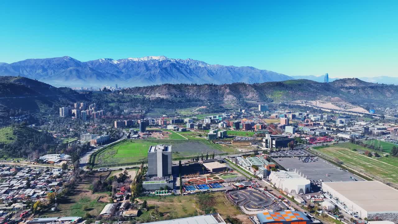 Orbiting drone aerial of Huechuraba district, Santiago, Chile with majestic snow-capped Andes mountains, urban landscape and valley panorama