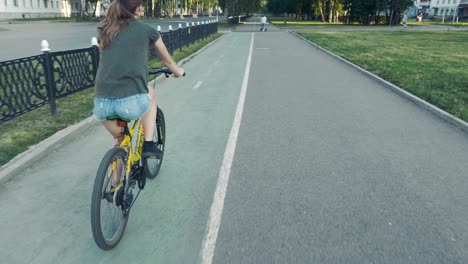 side view of a girl cycling on a road with flowers in a basket and exploring the city, slow mo, steadicam shot