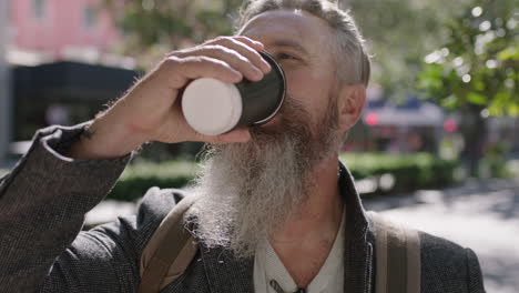 portrait of mature sophisticated bearded man drinking coffee beverage on city sidewalk enjoying happy urban lifestyle