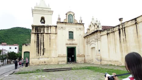 Female-in-white-top-taking-photograph-of-Convento-San-,-Salta-lush-green-mountain-range-in-background