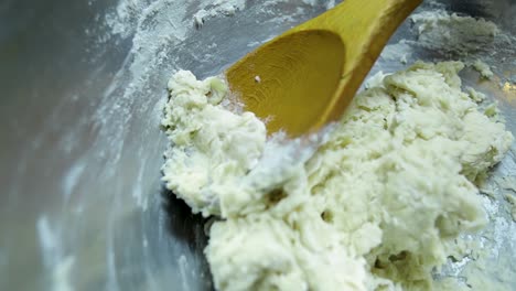 close up view of pizza dough siting in a silver pan next to a wooden spoon as the camera slowly turns circling the food