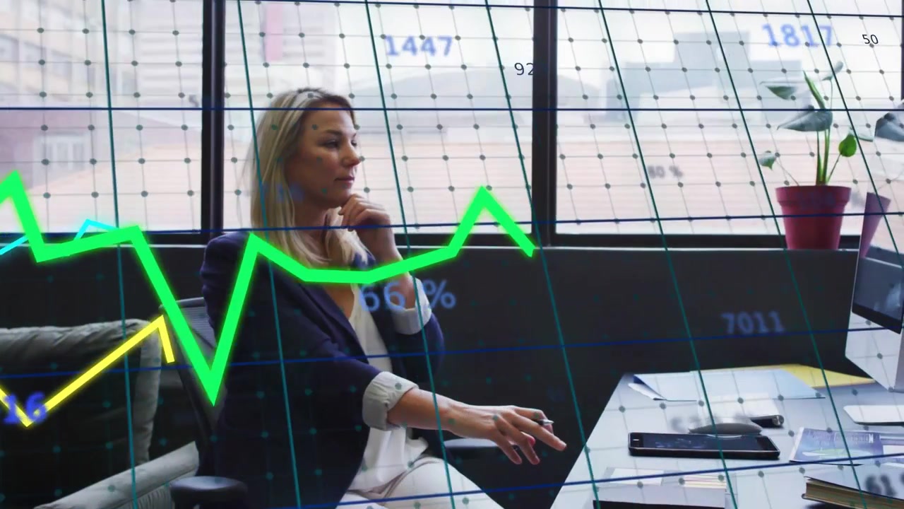 Donna seduta alla scrivania vicino alla finestra che digita e fa aggiornare grafici finanziari in tempo reale per l'analisi di mercato