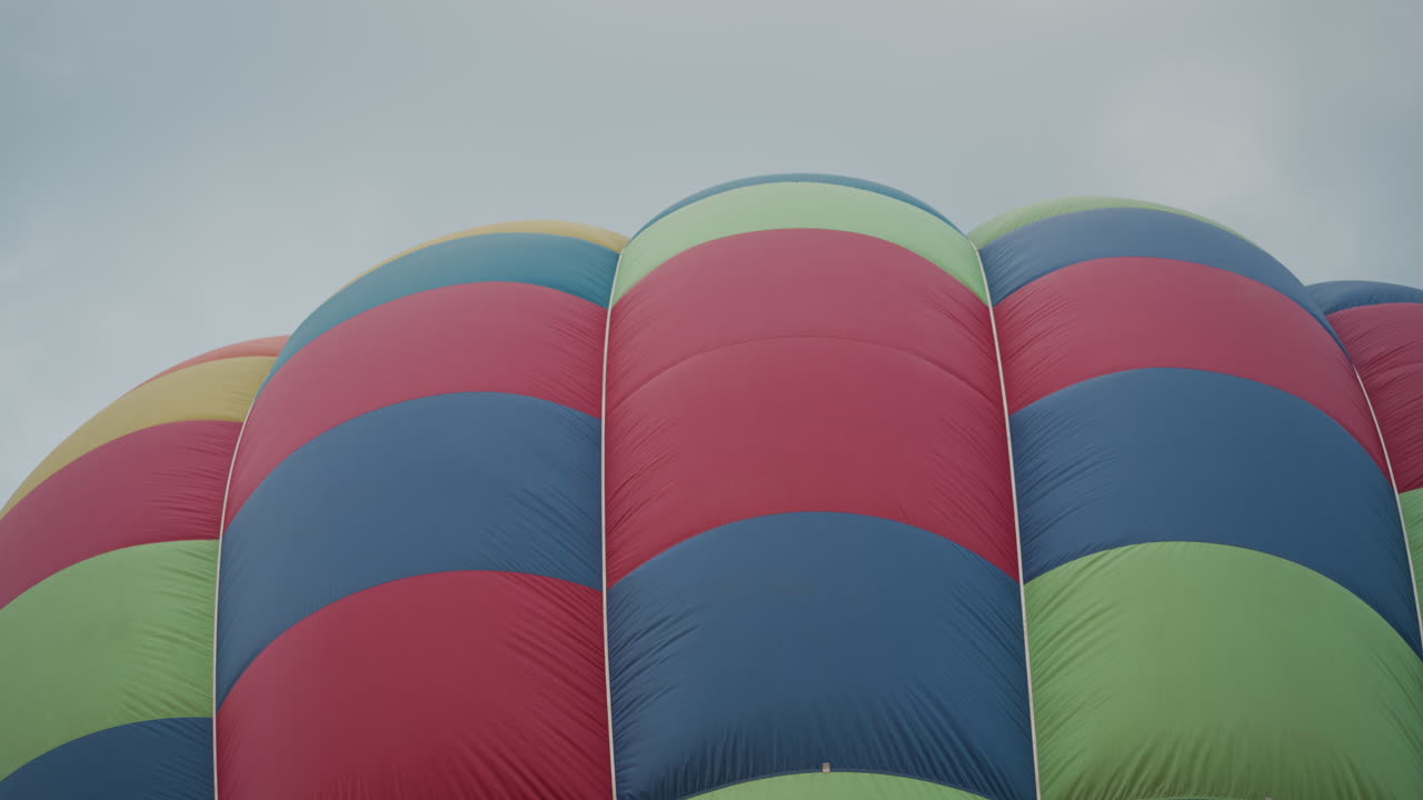 checker patterned hot air balloon envelope rising as warm air inflates vibrant panels against soft sky, rhythmic arcs of fabric capturing preparation energy before canopy ascends above field