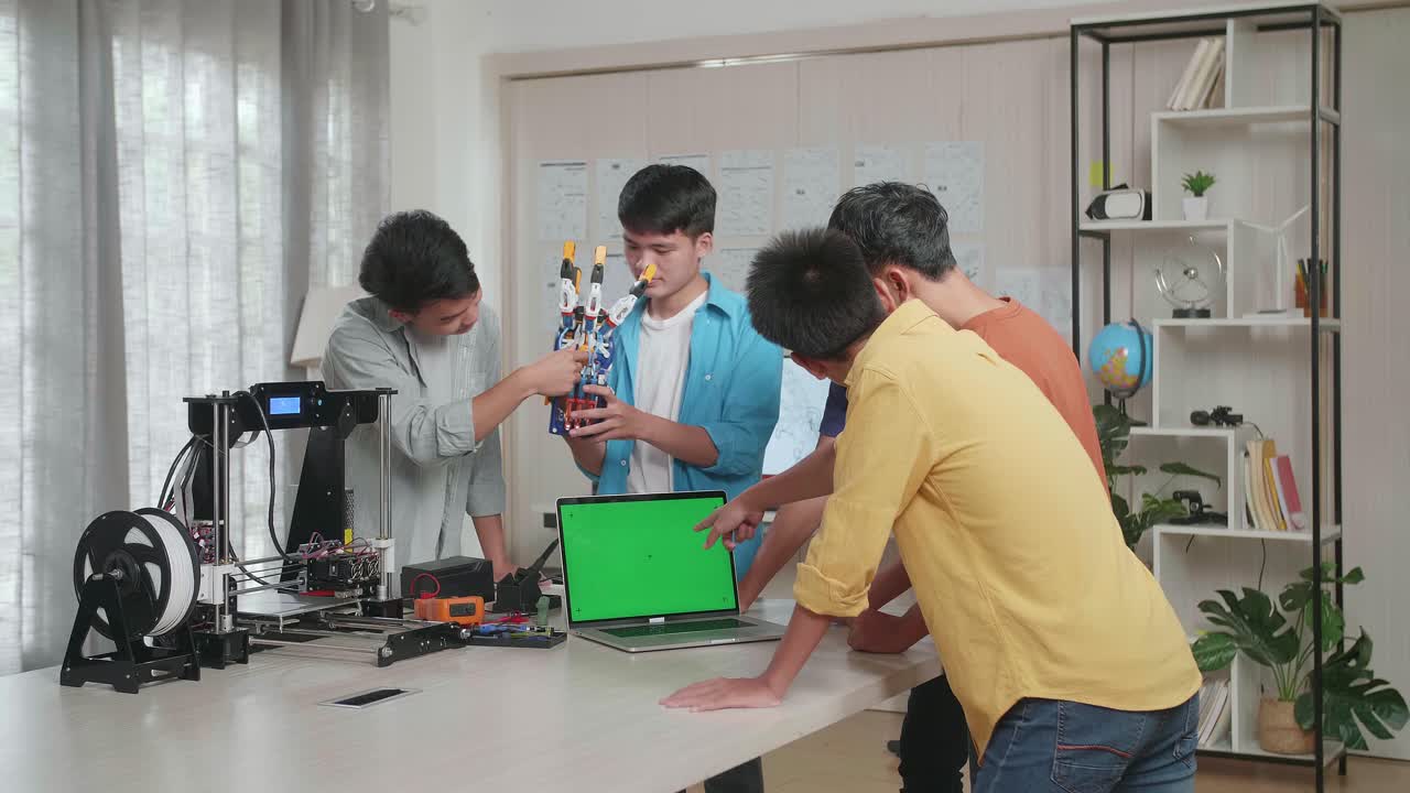 집에서 사이보그 손에 대해 작업하는 3d 프린팅을 가진 젊은 아시아 소년 그룹, 두 소년이 그것에 대해 논의하는 동안 세 소년은 모형 녹색 화면으로 노트북에서 일하고 있습니다.