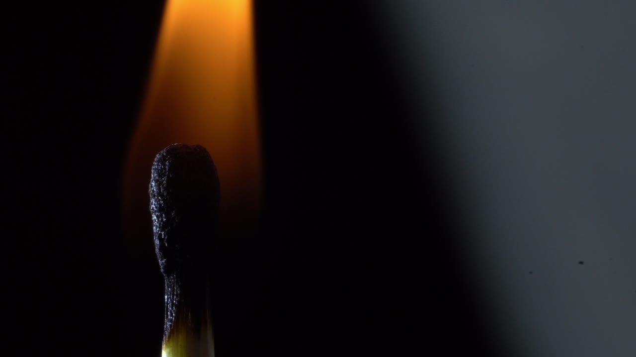 Burnt matchstick with a fading flame against a dark background