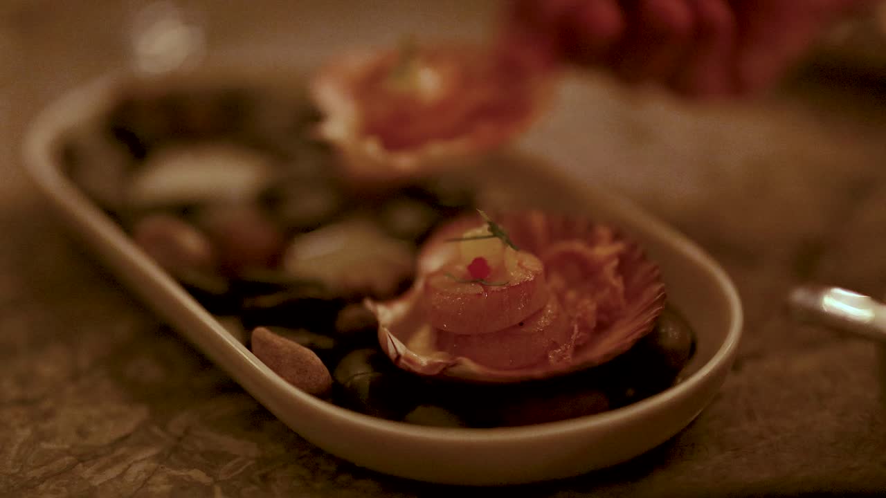 Hands delicately arrange grilled scallops on a platter. Warm lighting creates an inviting, elegant dining atmosphere