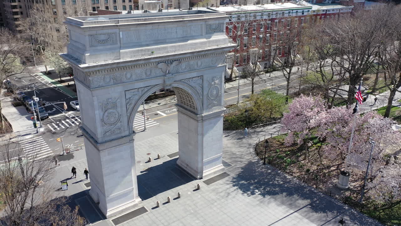 An aerial, day time view of the Washington Square Arch. The drone orbits the arch, counterclockwise with the very empty Washington Square Park - streets in view.