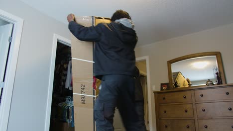 low angle shot of delivery drivers shuffling heavy cardboard box into bedroom box placed on the ground