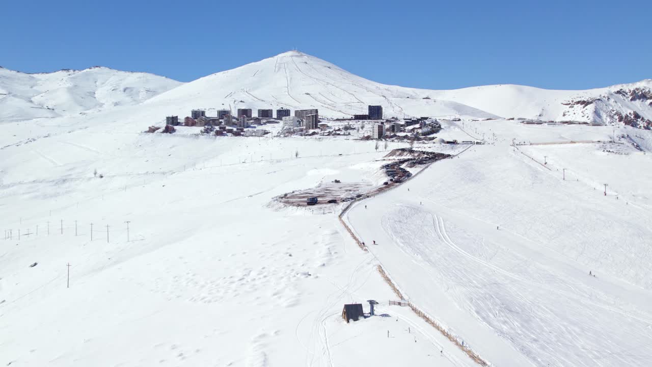 vista aérea rodeando la estación de esquí de farellones en la empinada ladera del valle montañoso cubierto de nieve de santiago, chile