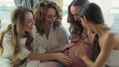 group of smiling adult women at baby shower touching bell of pregnant woman.