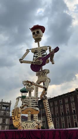 giant skeleton sculpture with guitar celebrates day of the dead in mexico city under cloudy sky