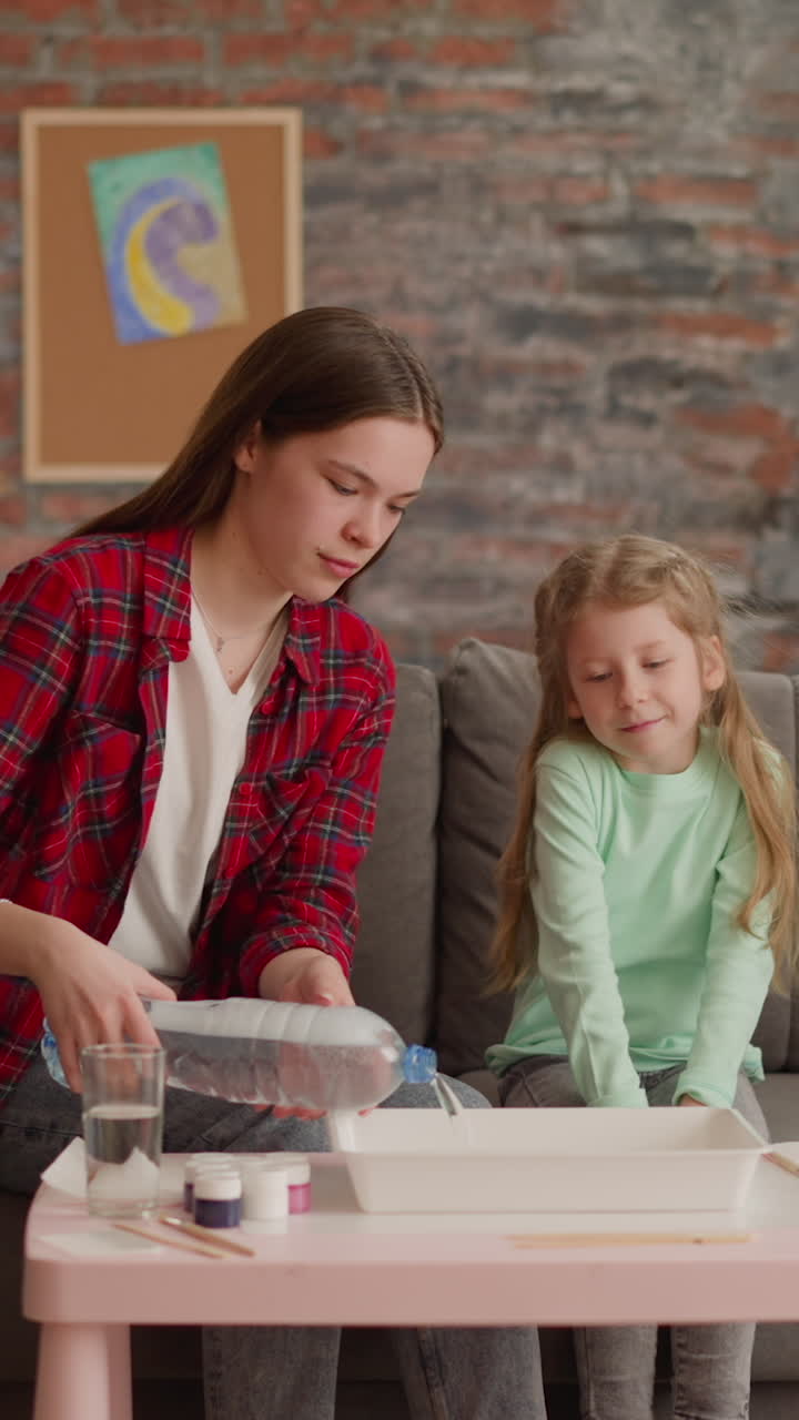 la hermana mayor vierte agua en la bandeja para el dibujo de ebru con la niña en la mesa en la sala de estar. familia en la lección de arte. pasatiempo creativo y ocio