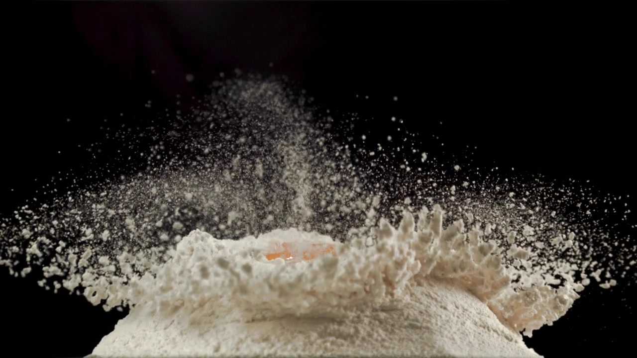 Slowmotion: Æggeblomme falder ned på en bunke mel.