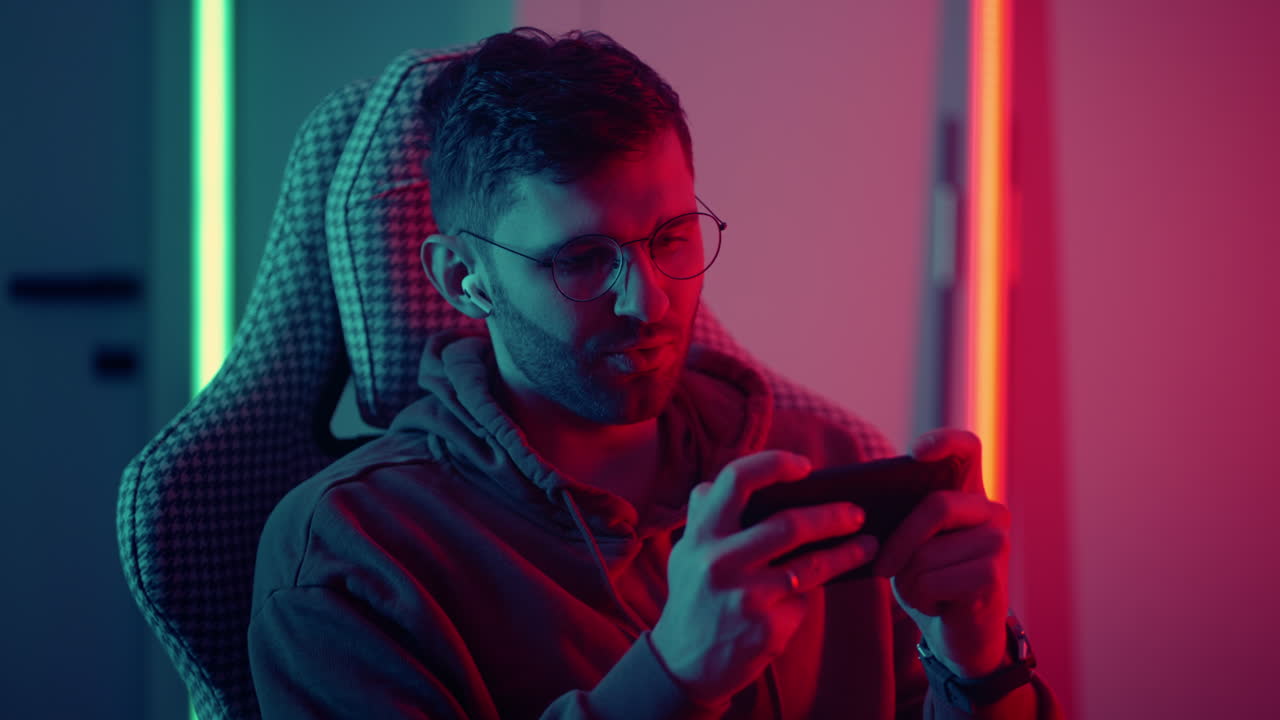 joven jugando a un juego móvil con su teléfono inteligente en casa por la noche adicto a internet jugador de ocio y entretenimiento disparando videojuegos ciberdeportivo en línea