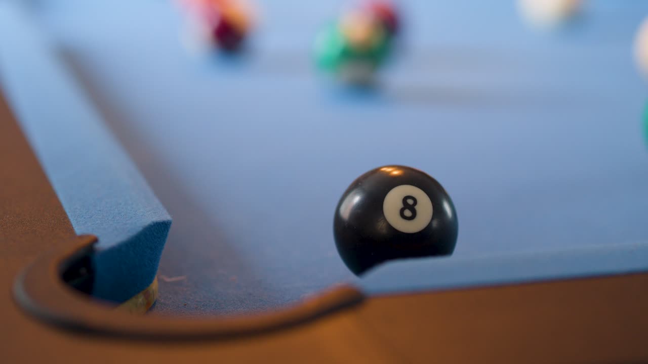 Eight ball and cue ball move on blue pool table, shallow focus, natural lighting