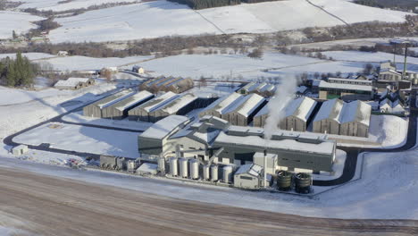 Aerial-view-of-the-Glenlivet-whisky-distillery-surrounded-by-snow-in-the-late-afternoon-sun-on-a-winters-day,-Moray,-Scotland---tracking-right-to-left