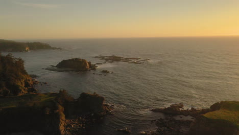 drone flying backwards over beautiful sea stacks and revealing cape arago lighthouse to the right