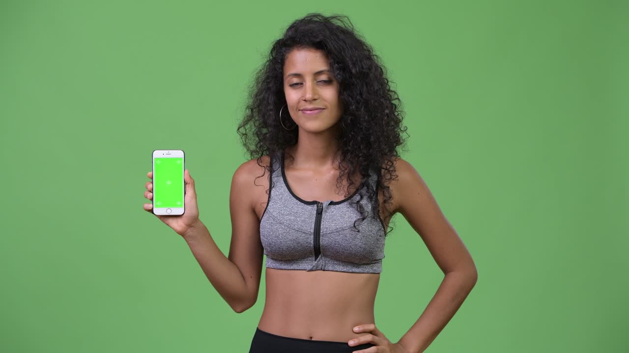 Young beautiful Hispanic woman with gym clothes showing phone
