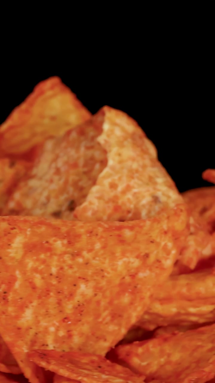 Chips di tortilla nacho dorate ruotano sotto l'illuminazione da studio, evidenziando la consistenza croccante e i dettagli della conditura