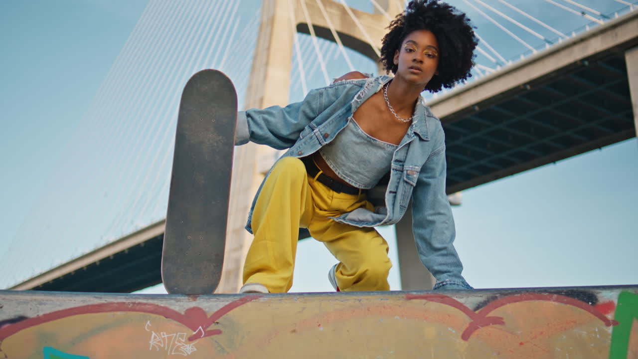 Chica radiante posando con el monopatín en un puente urbano. Patinadora sentada en la calle.