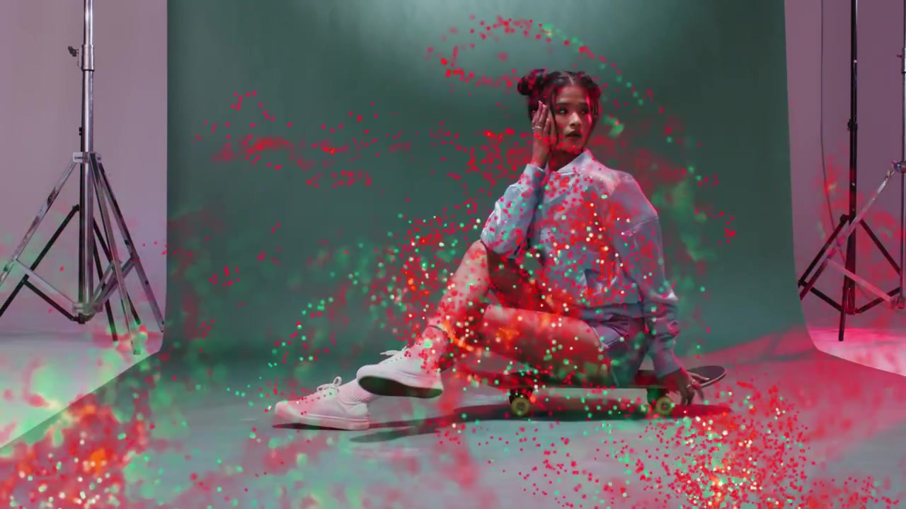 Modella asiatica in posa seduta su uno skateboard in studio con uno sfondo verde, con felpa con cappuccio e particelle rosse e verdi