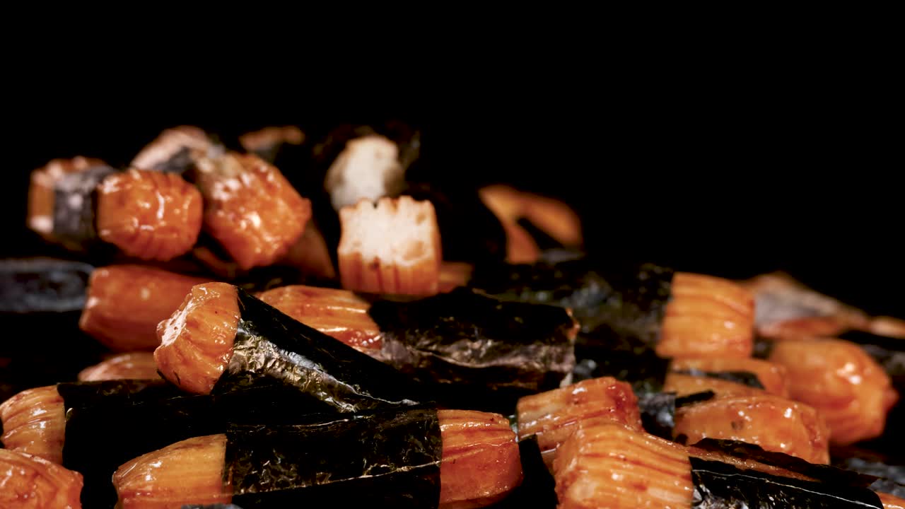 Macro shot rotates around crunchy Japanese rice crackers with seaweed, under dramatic studio lighting
