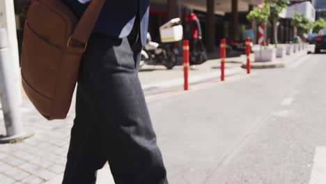 Midsection-of-african-american-businessman-holding-coffee-walking-in-city-street