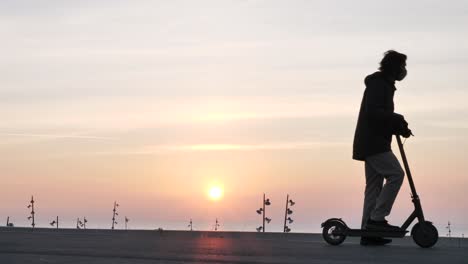 Silhouette-man-riding-electric-scooter-stops-to-admire-sunrise,-exits-right