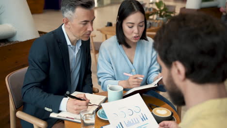 un equipo de trabajo analizando y comparando documentos y resultados en una reunión en una cafetería 1