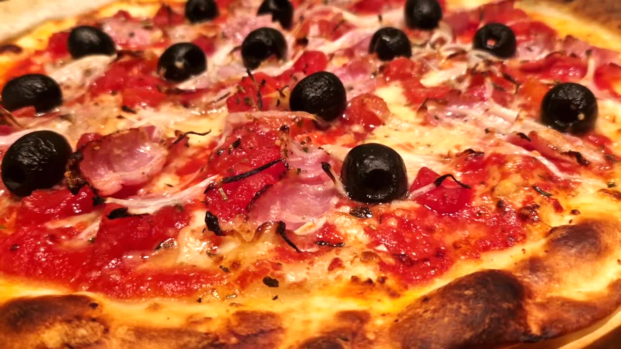 A mouth-watering close-up macro shot of a freshly baked homemade pizza, featuring a delightful combination of black olives, diced tomatoes, melted cheese, crispy bacon, and thinly sliced onions